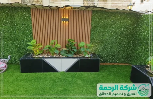 جلسات حديقة بالرياض 0559460943 شركة الرحمة منطقة جلوس خارجية مغطاة ببرغولا حديدية سوداء، تتميز بجدار خلفي يدمج بين الخشب والزرع الجداري بتصاميم هندسية