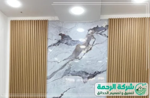 تركيب باب مخفي بديل الخشب بجدة 0559460943 الرحمة تصميم جداري داخلي مذهل يمزج بين الأخشاب الفاتحة والرخام، حيث تتوسط لوح رخامي كبير ذو عروق رمادية.